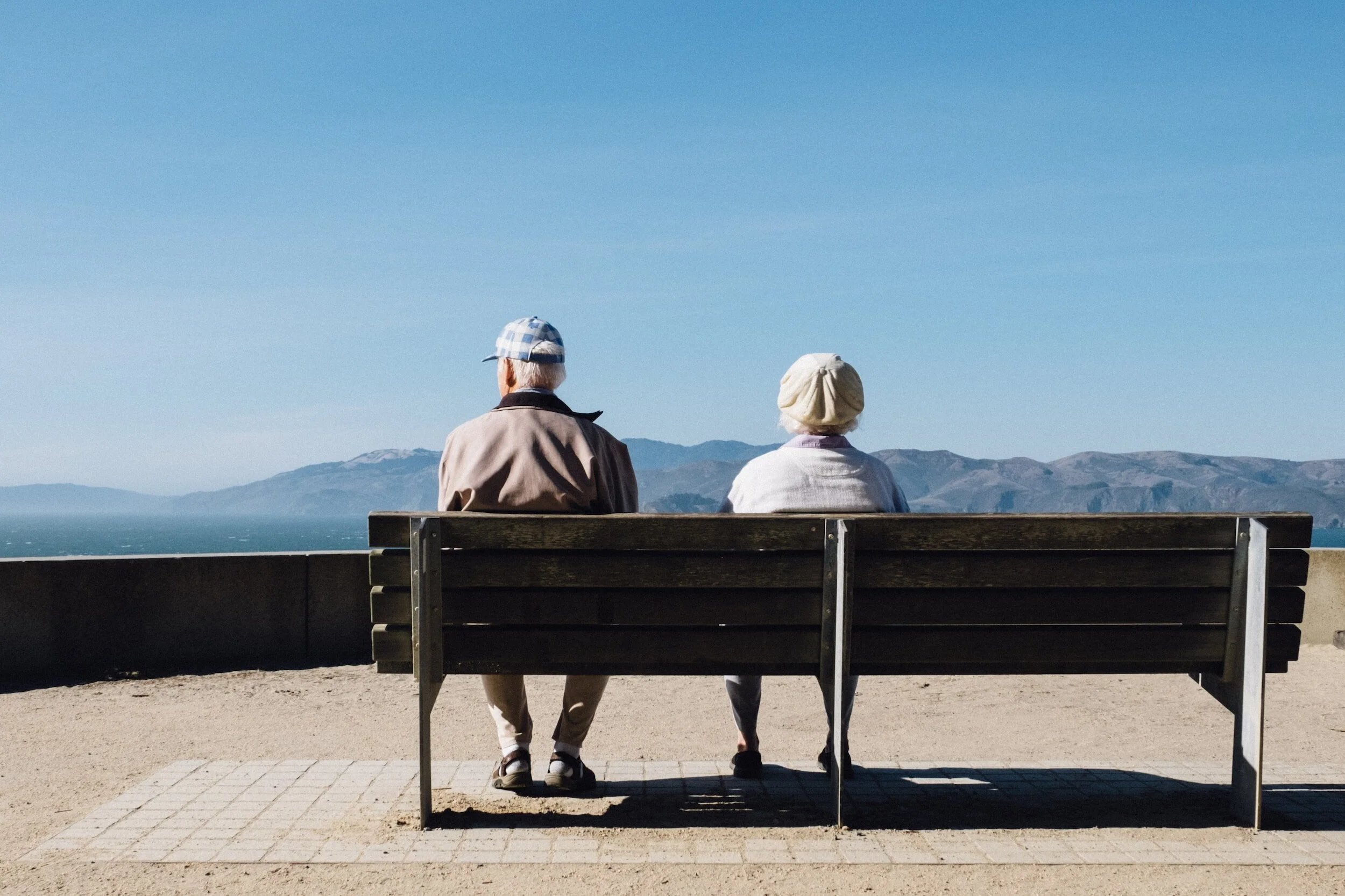 An older couple sitting on a bench overlooking the ocean